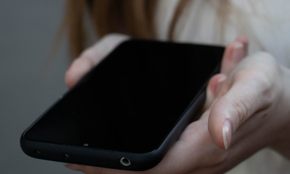 画面が暗いままのスマートフォンを手のひらにのせて持っている手元