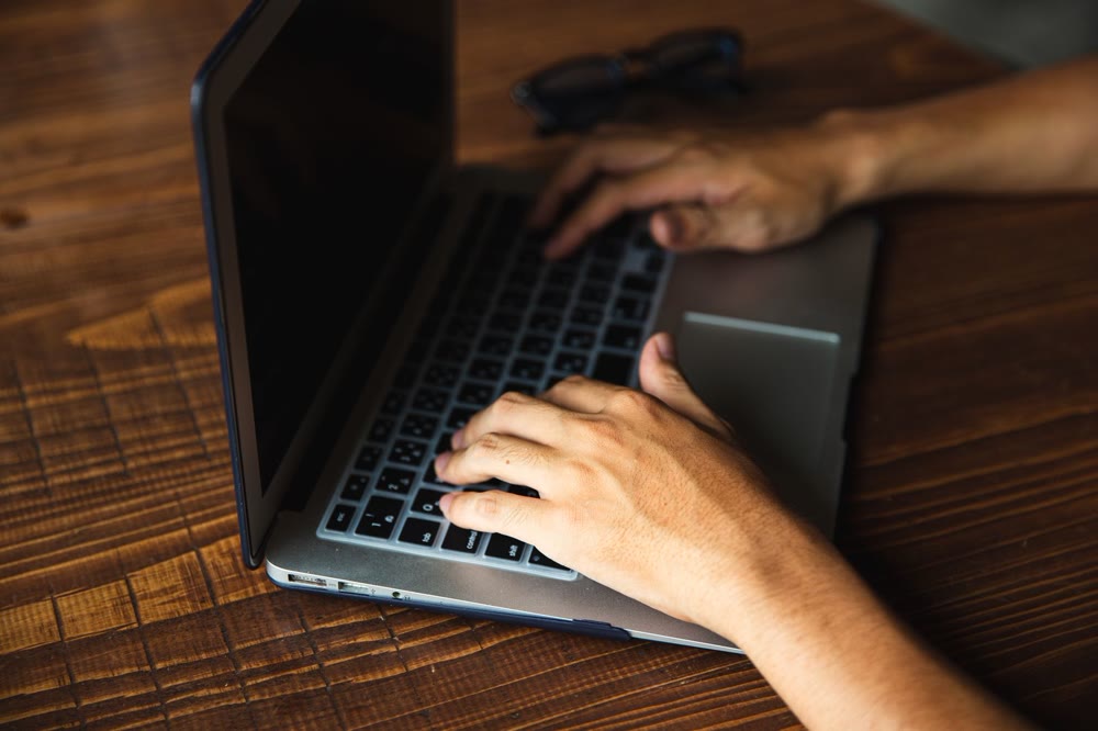 木の机でノートPCのキーボードに両手を置いて操作している手元