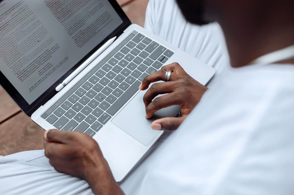 ノートパソコンの画面に並ぶ文書を読みながら、トラックパッドに指を置く手元