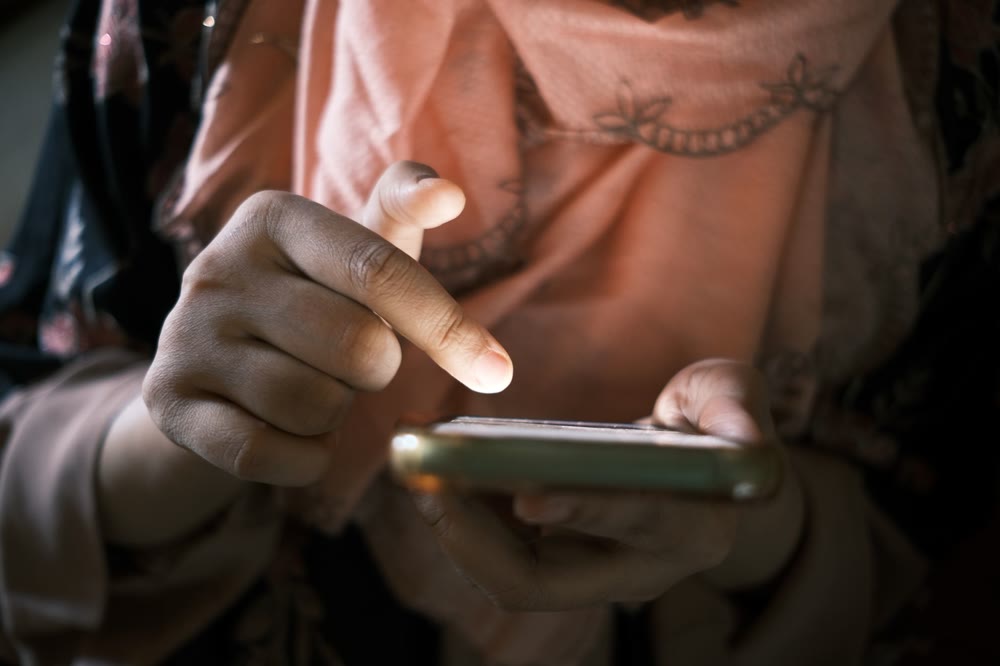 画面に向けて人差し指を伸ばし、スマートフォンをタップしようとしている手元