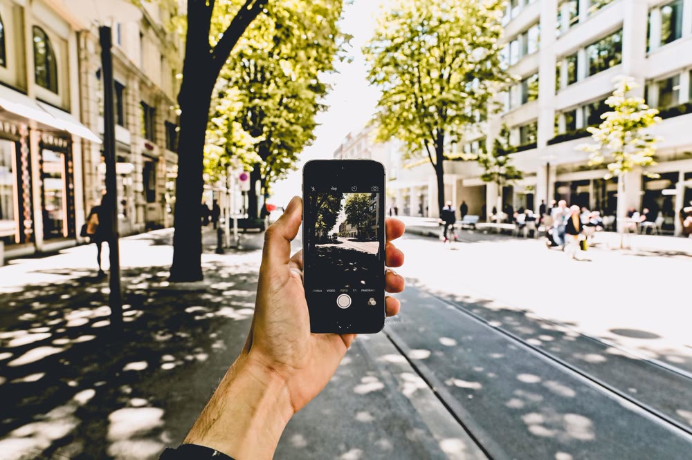 街なかの並木道で、スマートフォンのカメラを向けている手元