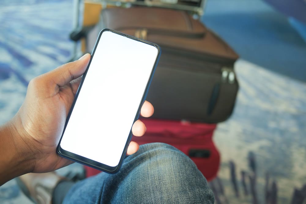 スーツケースを脇に置き、スマートフォンを片手で持っている手元
