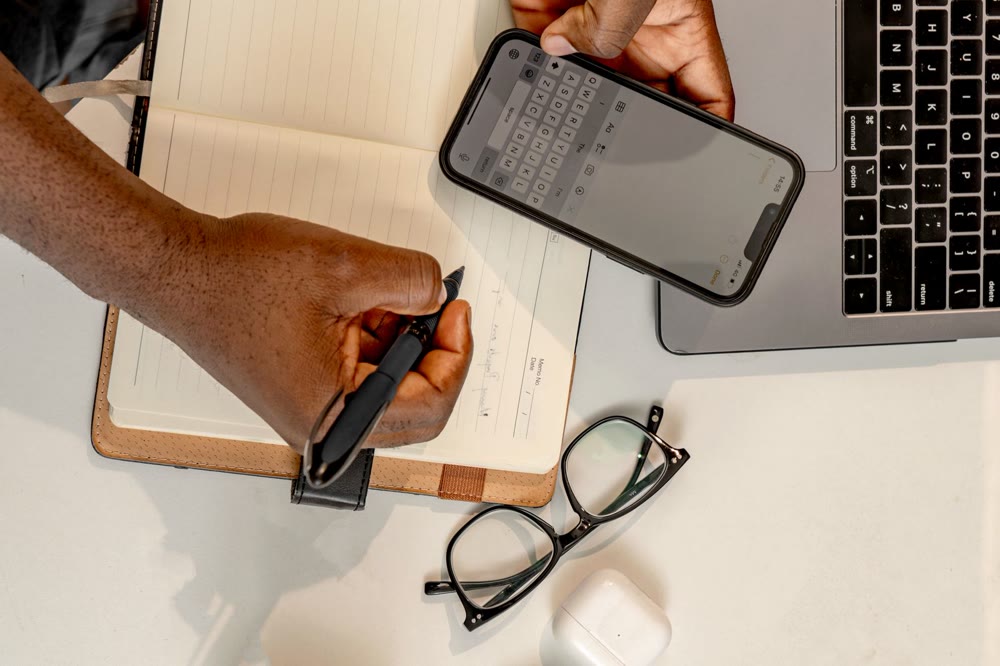 スマートフォンを手に、ノートに書き込んでいる人を真上から見た手元