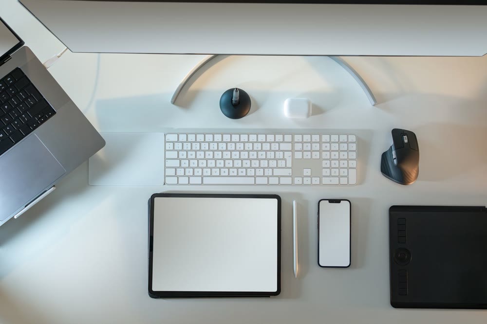 机の上にタブレットとスマートフォン、キーボード、ノートパソコンの端が並んでいる様子を真上から見たところ