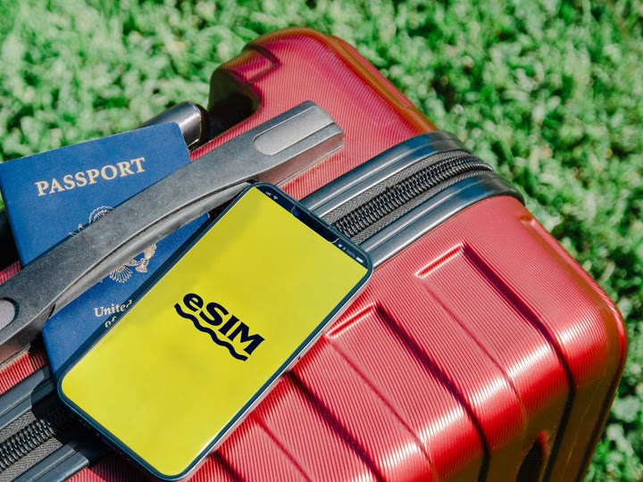 赤いスーツケースの上に置かれたパスポートと、eSIMの文字が表示されたスマートフォン