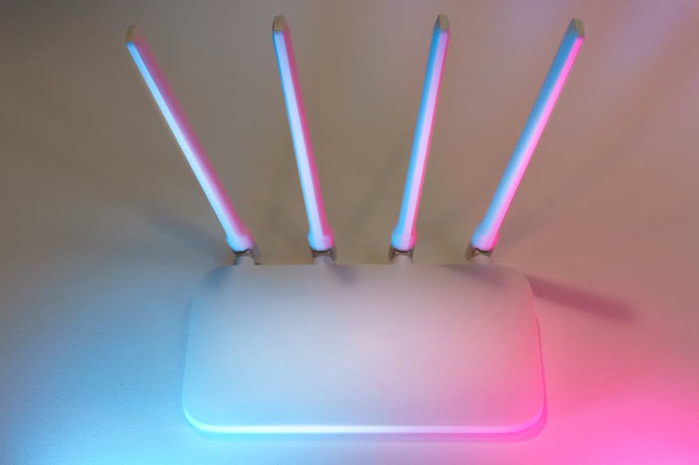 淡い水色とピンクの光に照らされた、アンテナが4本ある白いWi-Fiルーター