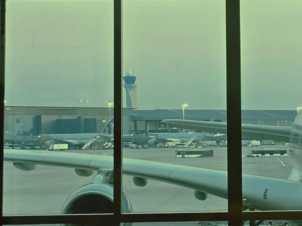 空港の窓越しに、駐機している大型旅客機の主翼とエンジン、奥の管制塔が見える様子