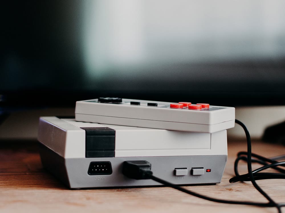 ぼやけたテレビの前の木の台に、レトロなゲーム機本体とその上に載せたコントローラーが置かれている