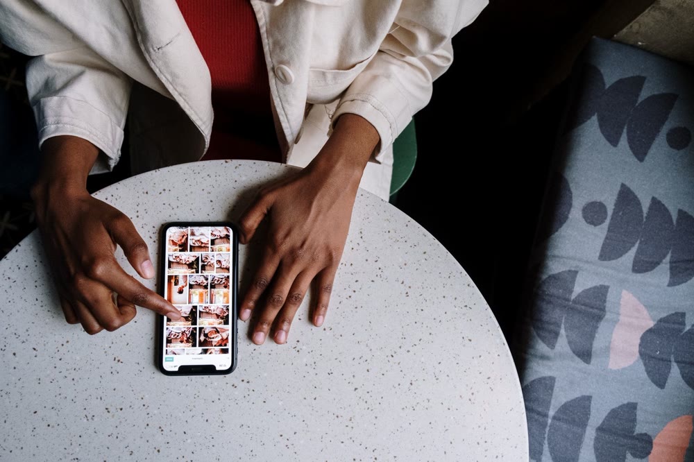 カフェの丸いテーブルに置いたスマートフォンの画面を、指で操作している手元