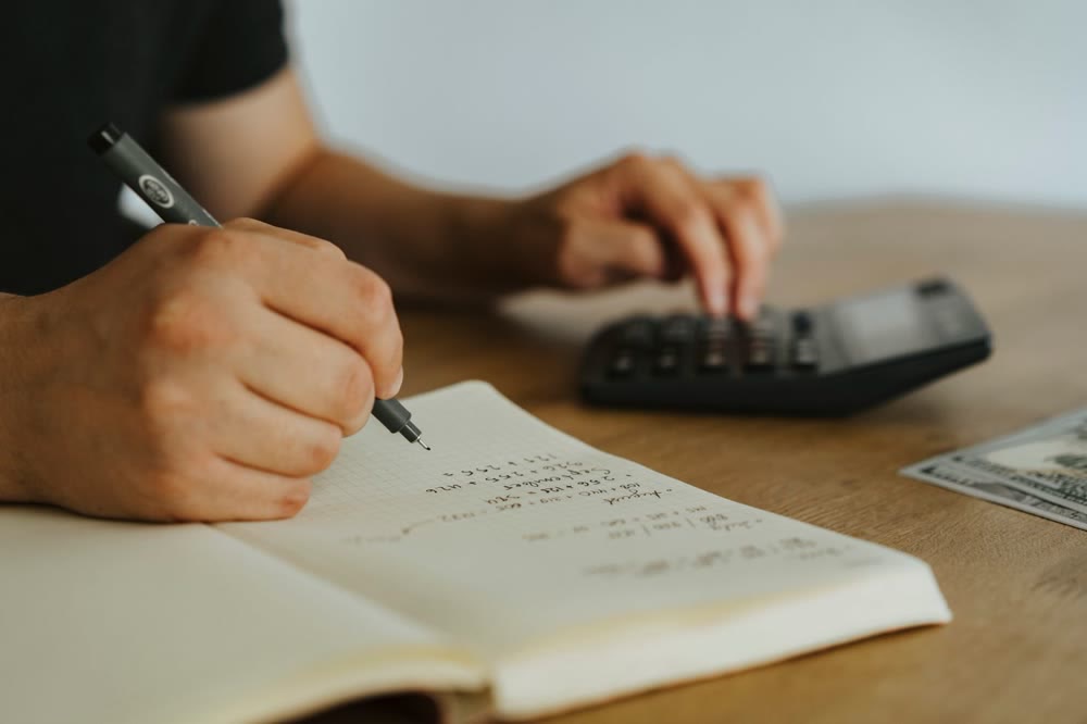 手書きのノートに数字を書き込みながら、電卓を使って計算する手元