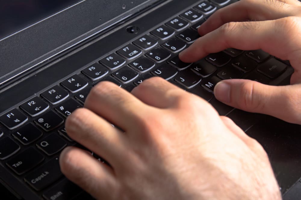 ノートパソコンの上段のファンクションキーが見える位置で、キーボードに両手を置いている手元