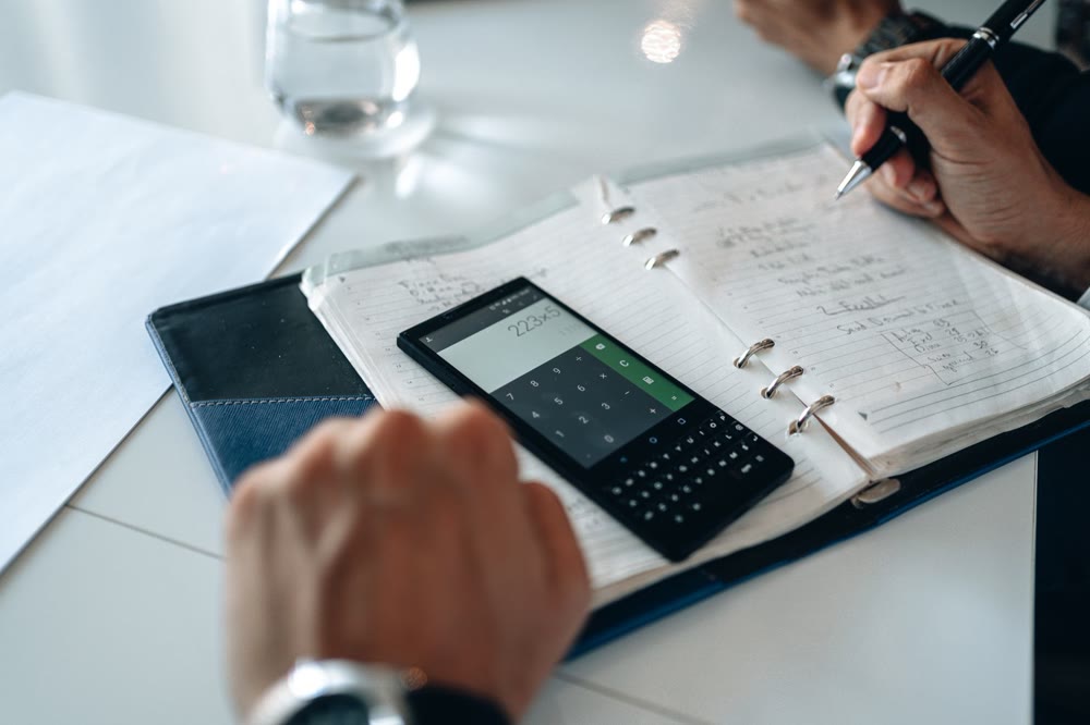 電卓を表示したスマートフォンとノートを前に、支払いを計算している二人の手元