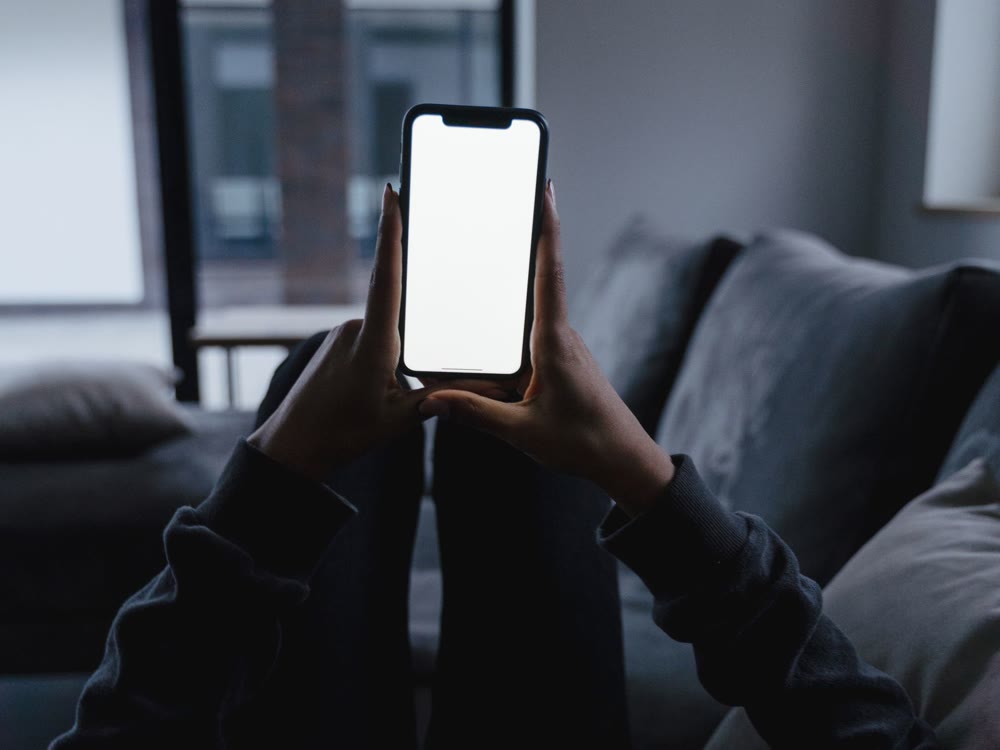 ソファに横になって、両手で持ったスマートフォンの画面を見ている様子