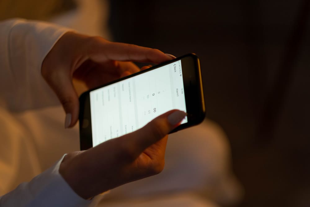 スマホの画面を両手の指で操作して、設定項目を順に探している手元