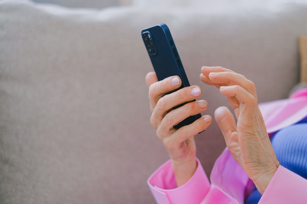 ソファに座った人が、スマートフォンを片手で持ち、もう一方の手を画面に近づけている手元