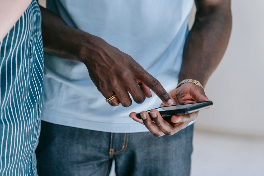 スマートフォンを持つ手と、その画面を指さしている手