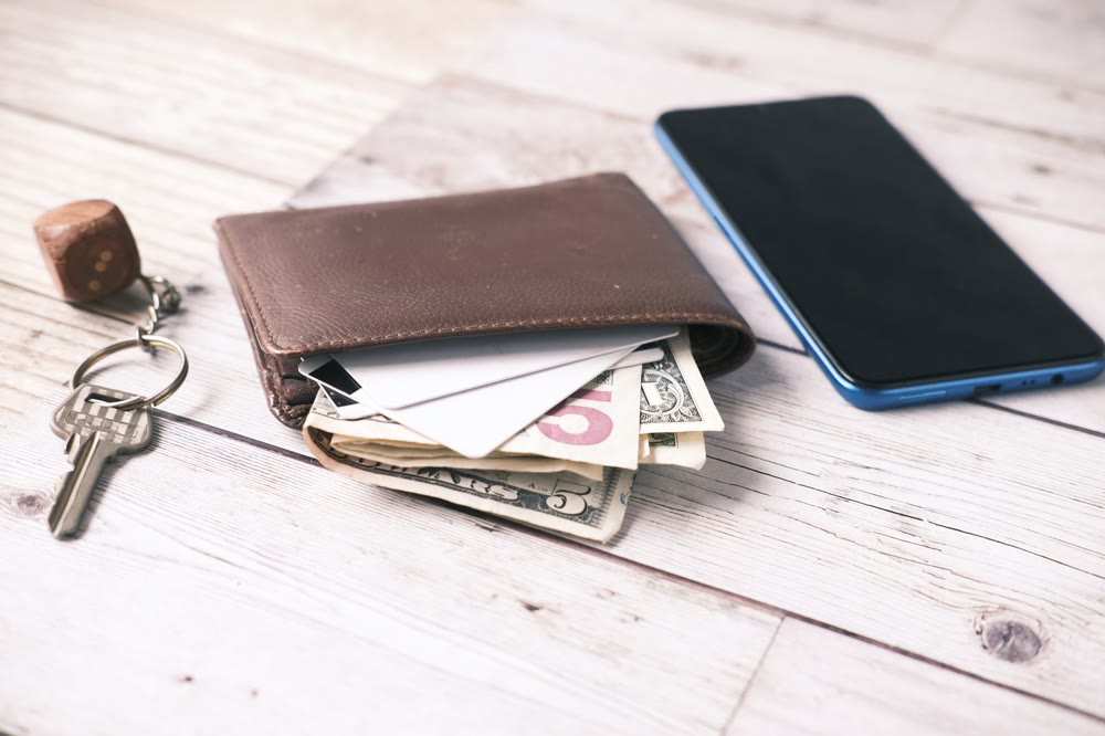 財布から覗くカード類とドル紙幣、横に置かれたスマートフォンと鍵