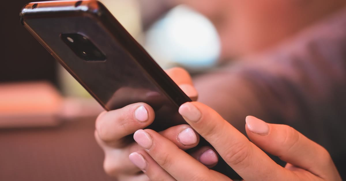 茶系のぼかした背景の前で、両手でスマートフォンを持って操作している手元